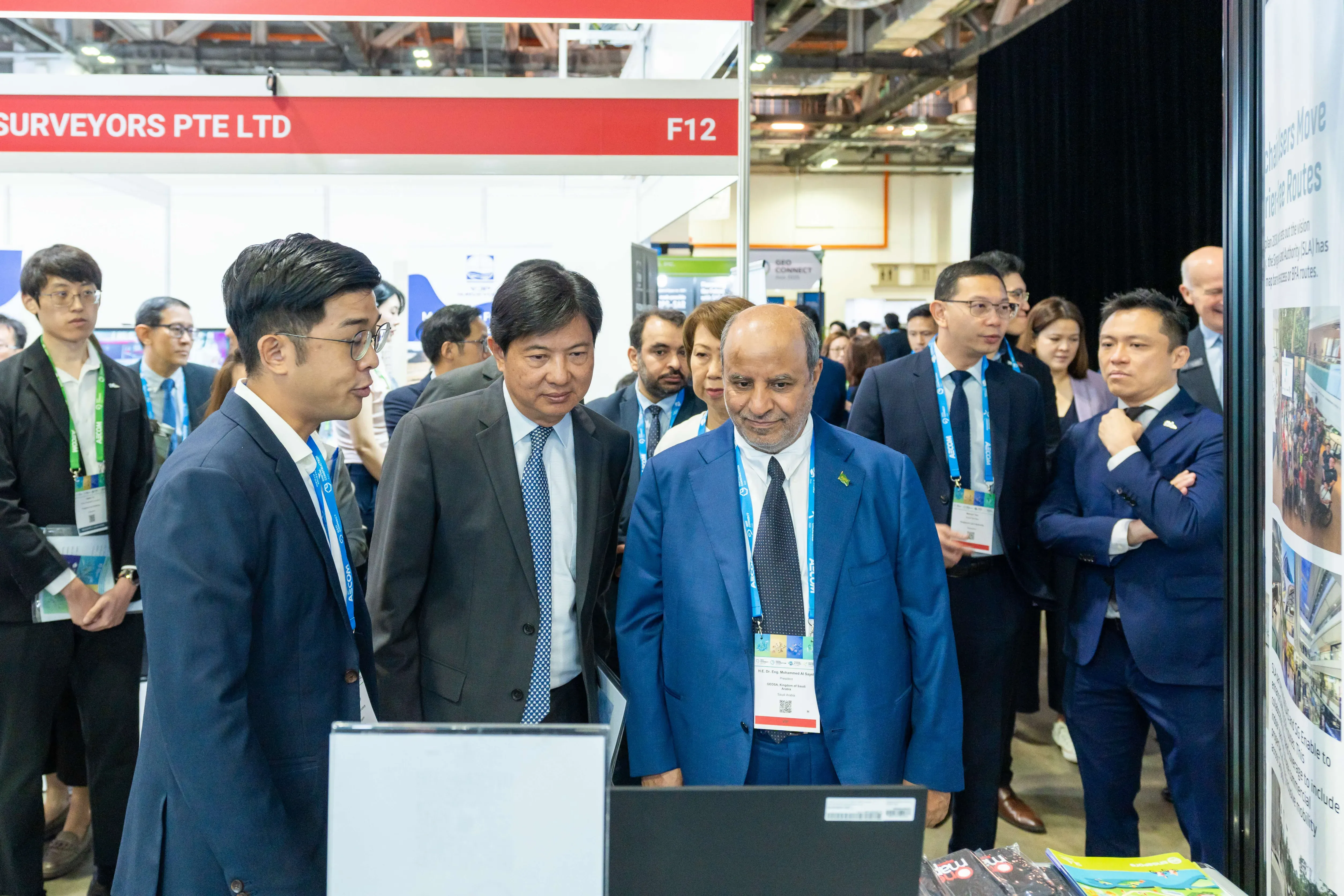 Several professionals in suits with lanyards gather at booth F12 of Surveyors Pte Ltd at a trade exhibition.